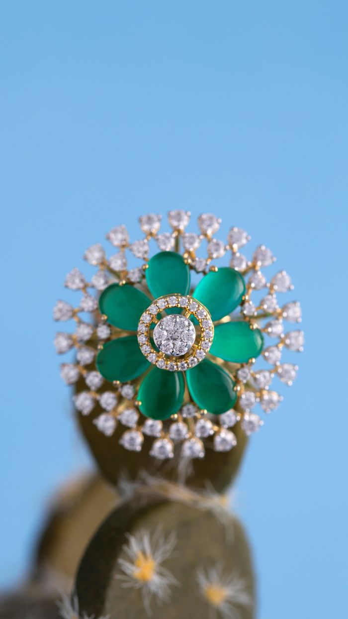 Gorgeous diamond and emerald ring displayed on a cactus against blue background.